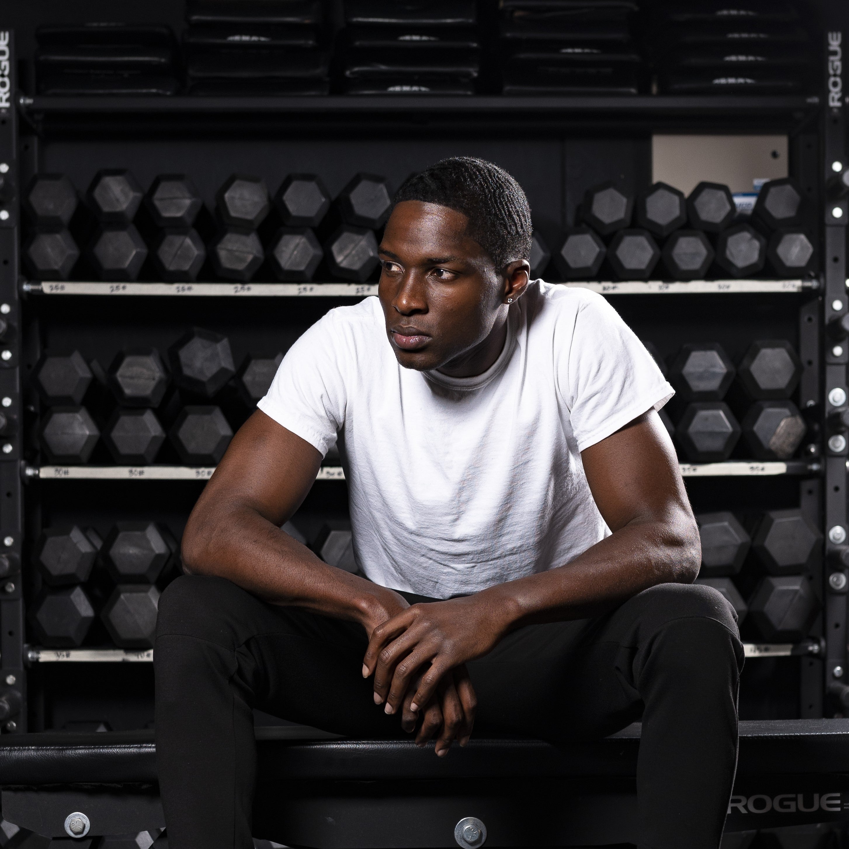 Athlete or crossfitter resting after a workout with dumbbell rack behind him. 